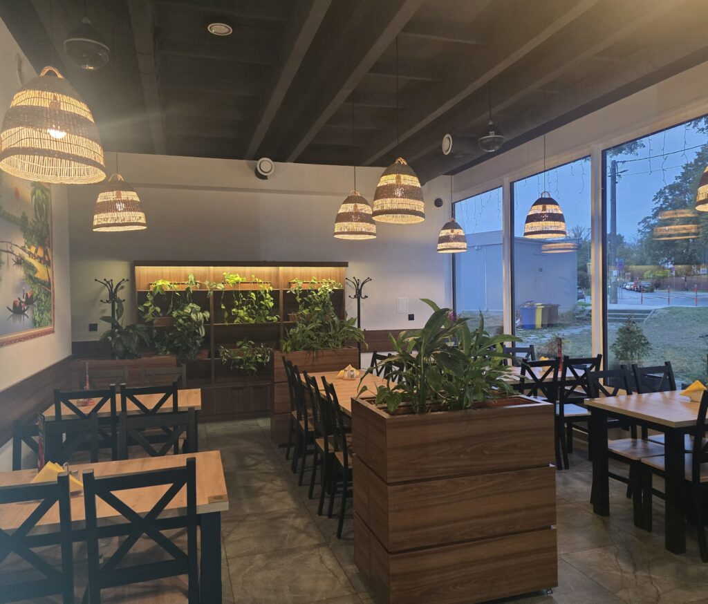 Wnętrze Bistro Kuchnia Polska – drewniane stoły, wiklinowe lampy i zieleń
